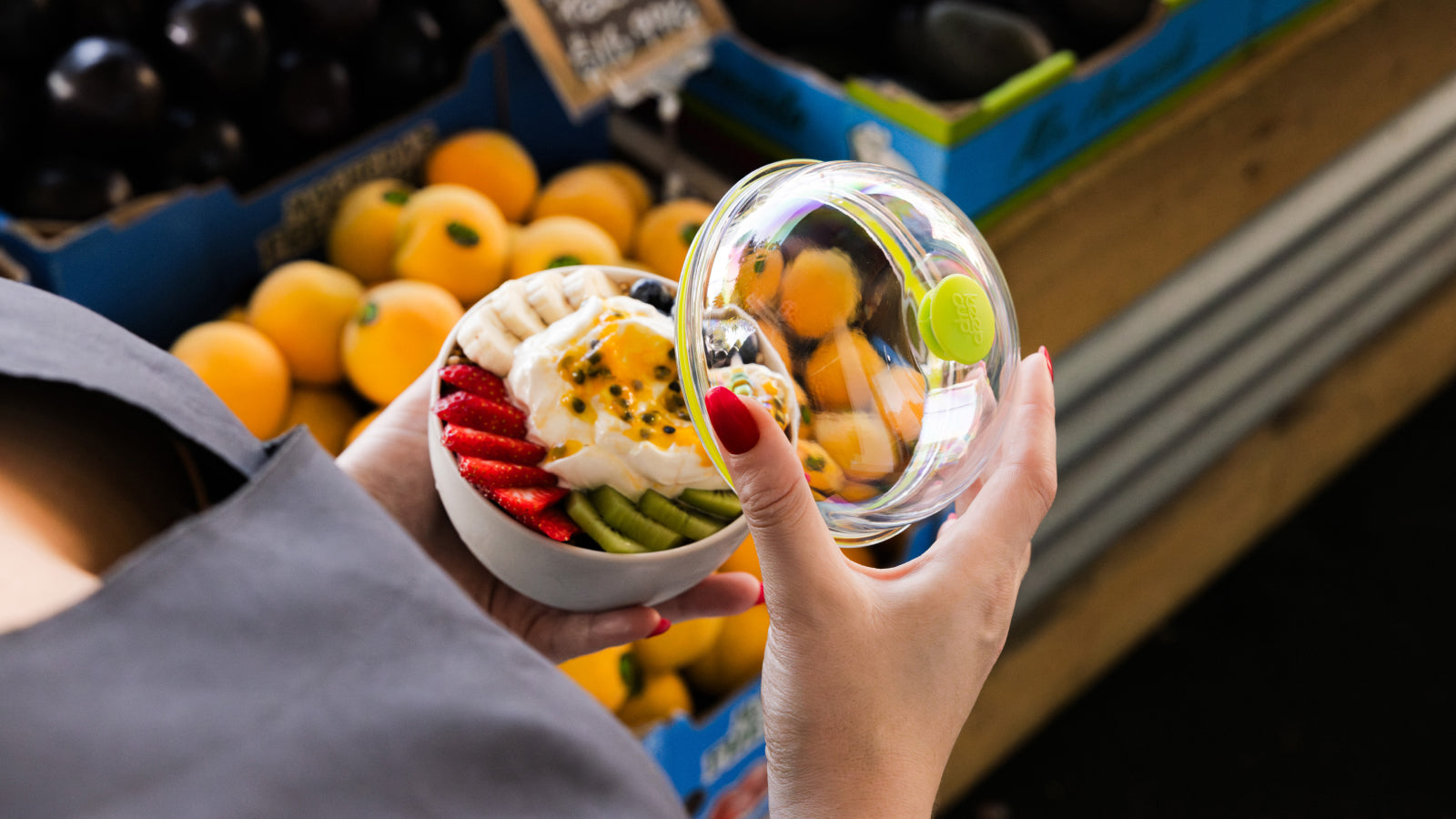 Womans hand holding acai filled KeepCup Go Bowl walking past fruit stall