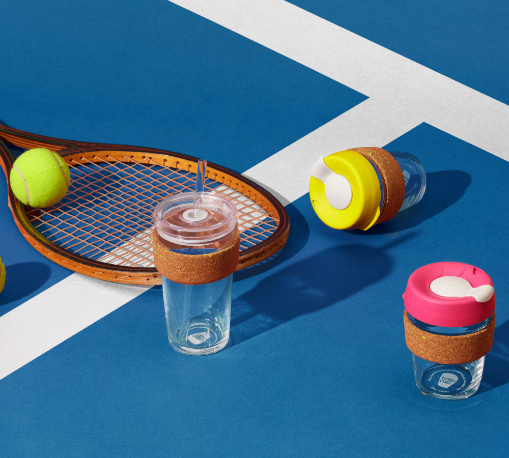 KeepCup Ace range cold up with tennis racquet on tennis court