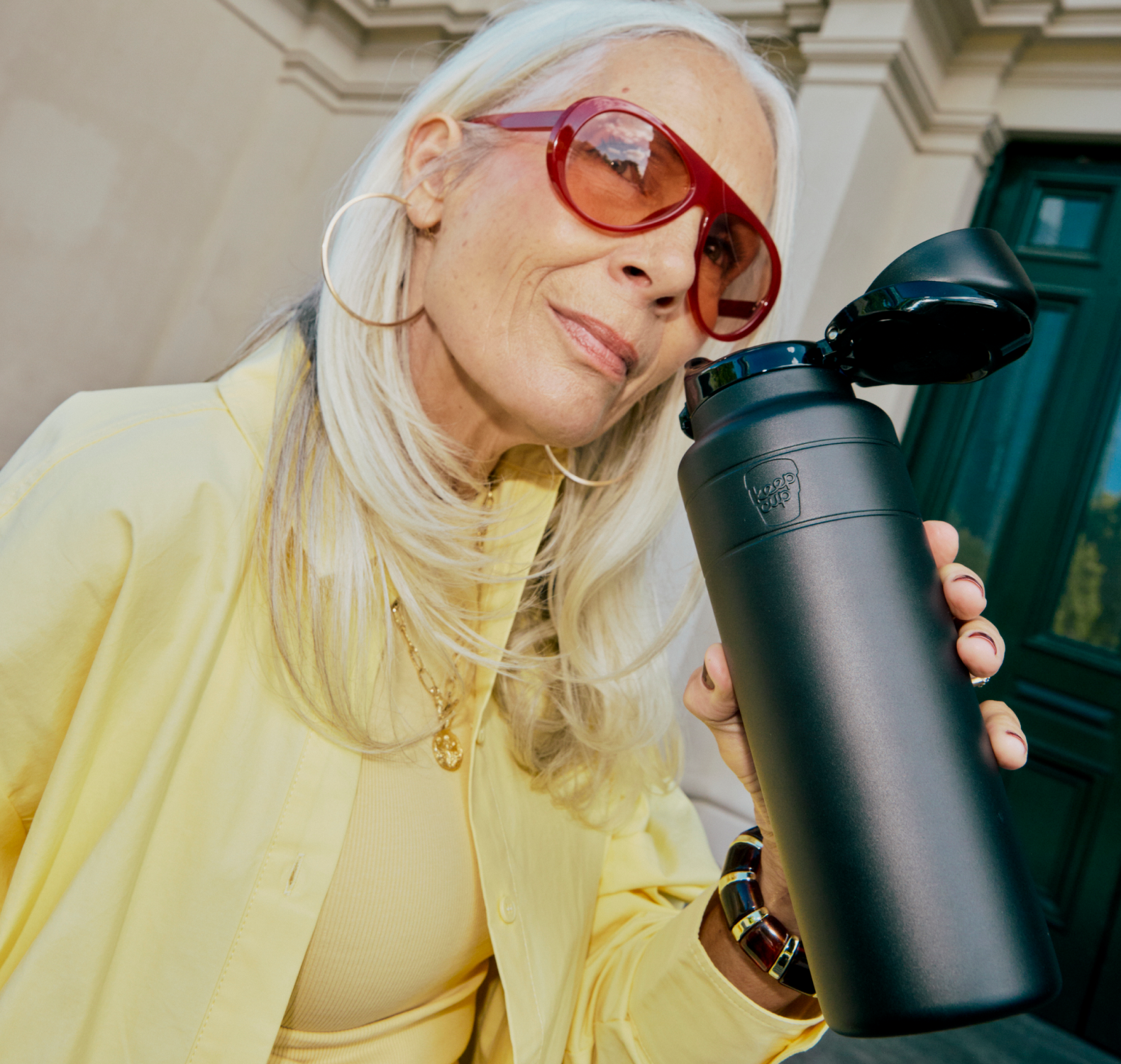 Woman in yellow with long gray hair holding black 950ml Ora Bottle