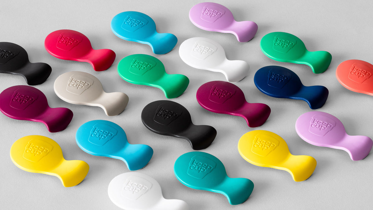 Colorful silicone phone grips in various bright colors including yellow, blue, green, pink, purple, red, black and white with embossed logo