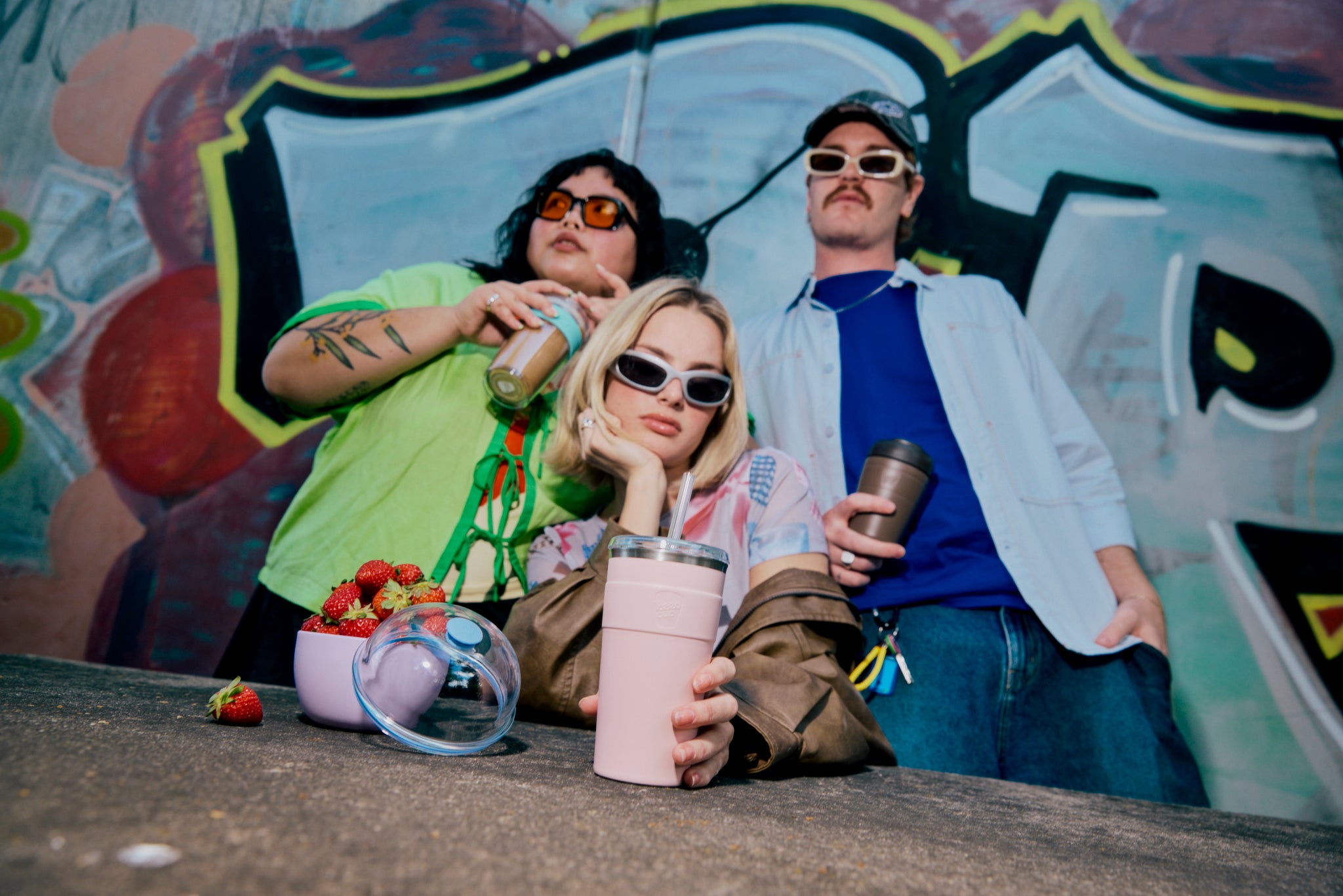 Three people posing with drinks against a graffiti-covered wall