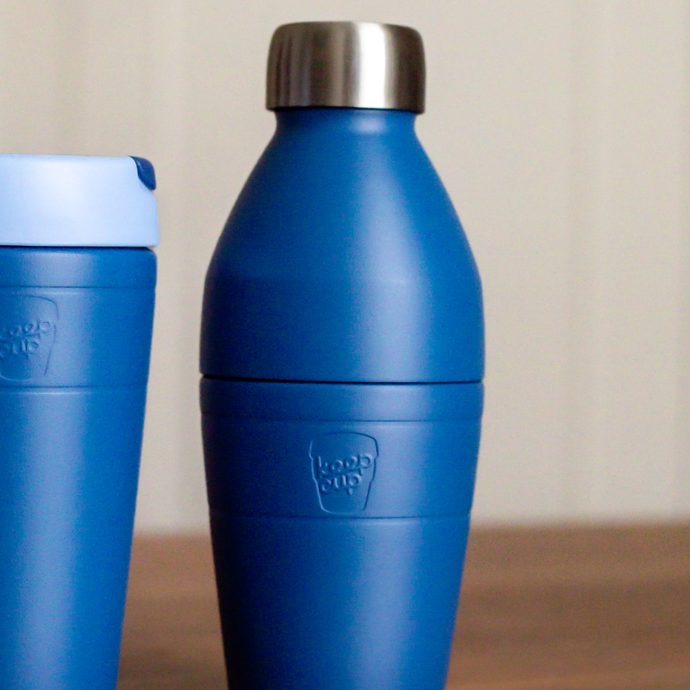 KeepCup blue insulated bottle with silver lid and Traveller cup in matching colourway on a wooden surface.