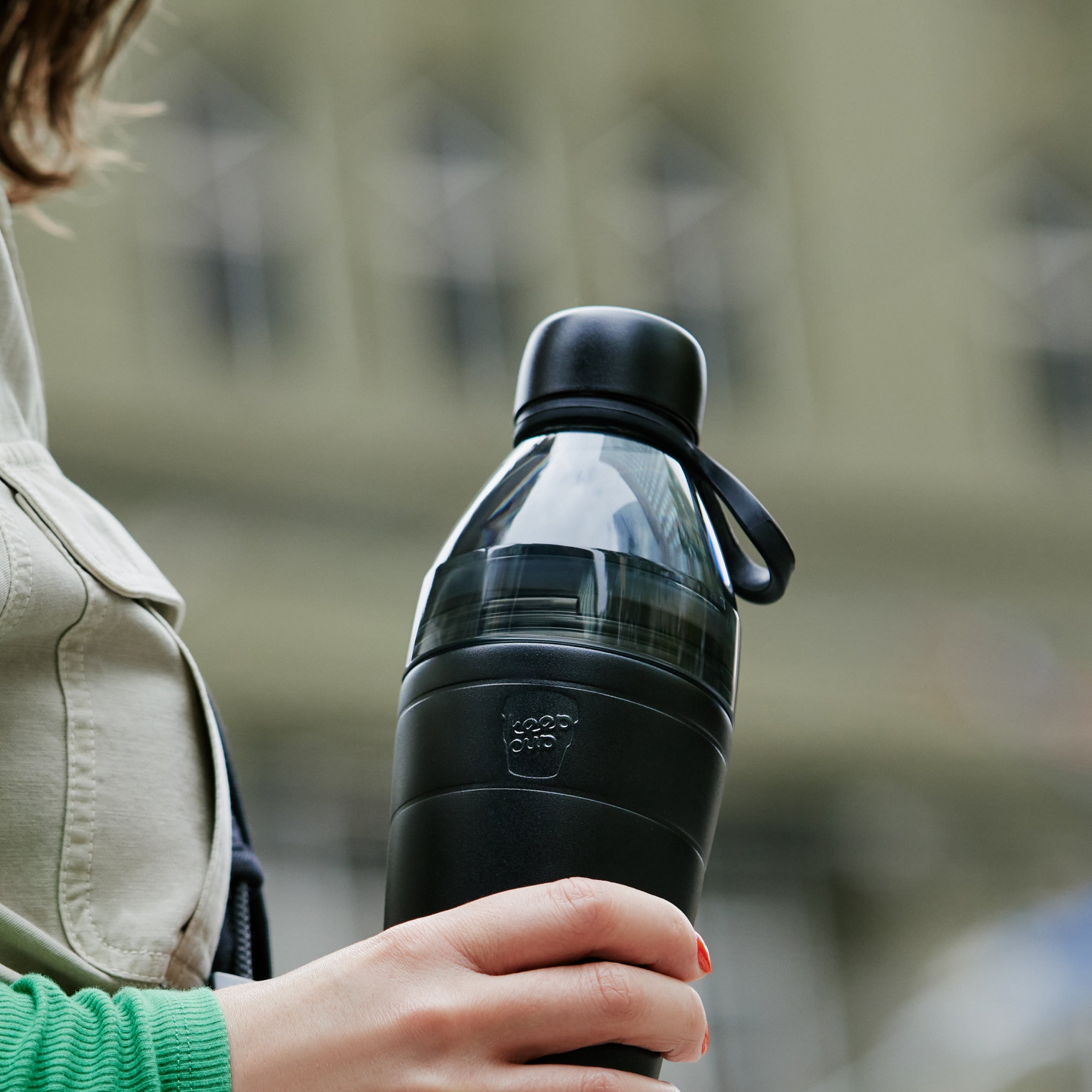 Person holding a black insulated KeepCup water bottle with a blurred background