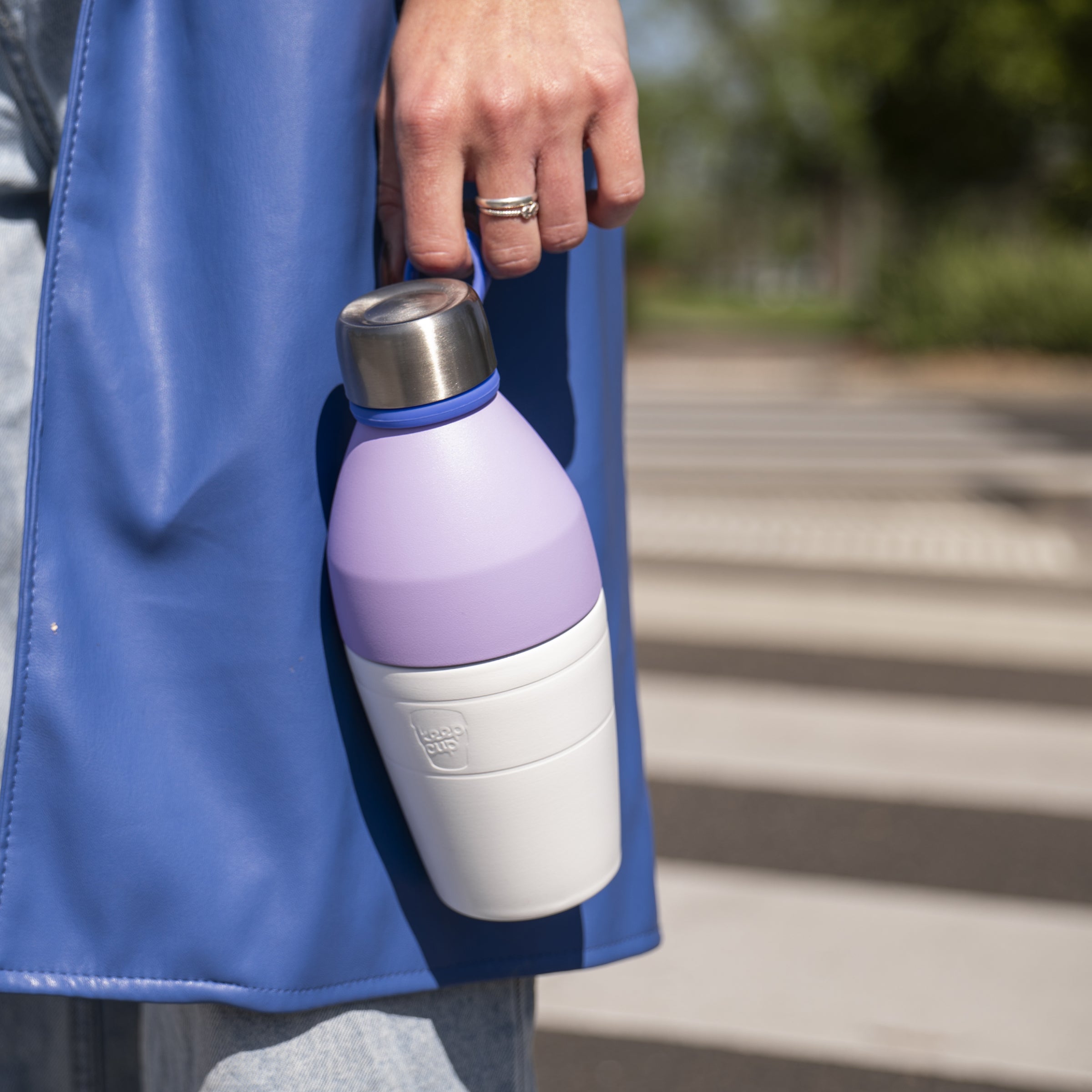 Person holding a purple and white KeepCup insulated bottle outdoors