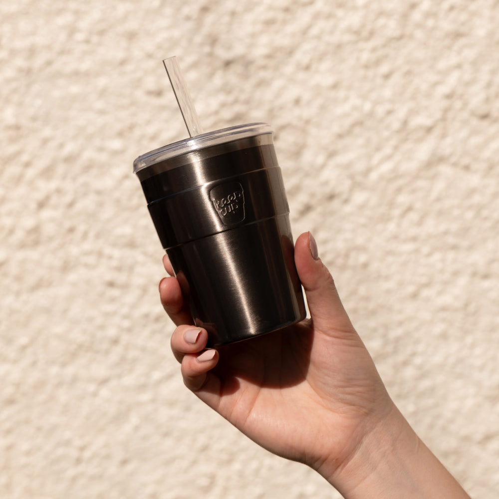 Hand holding stainless steel insulated tumbler with clear lid and straw against beige textured background