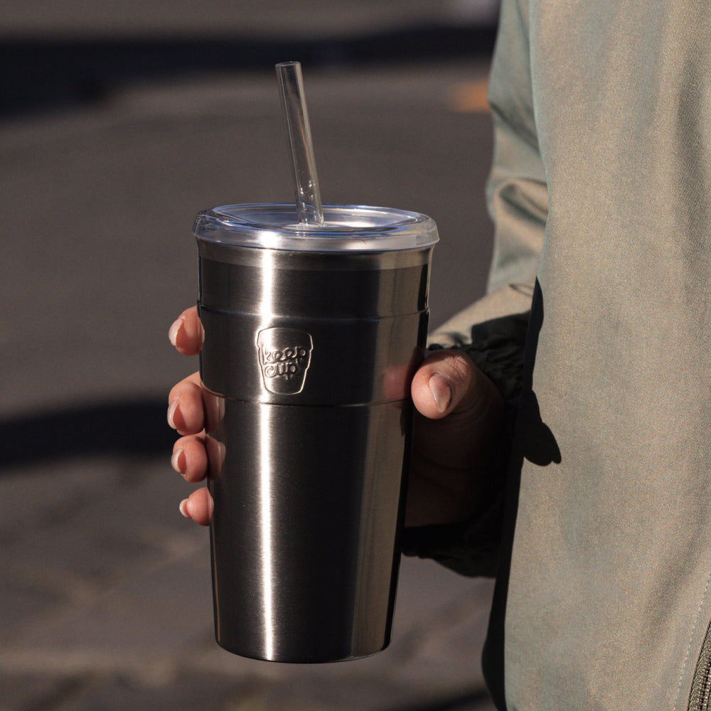 Person holding stainless steel insulated tumbler with clear lid and straw, featuring KeepCup logo