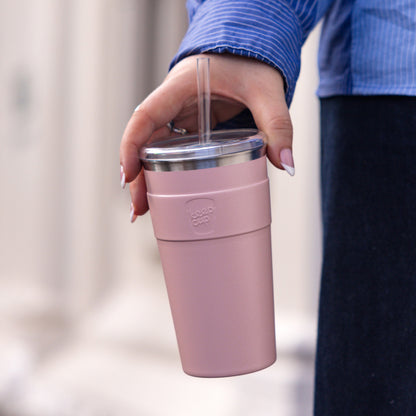 Person holding a pink reusable coffee cup with stainless steel lid and clear straw, wearing blue striped shirt