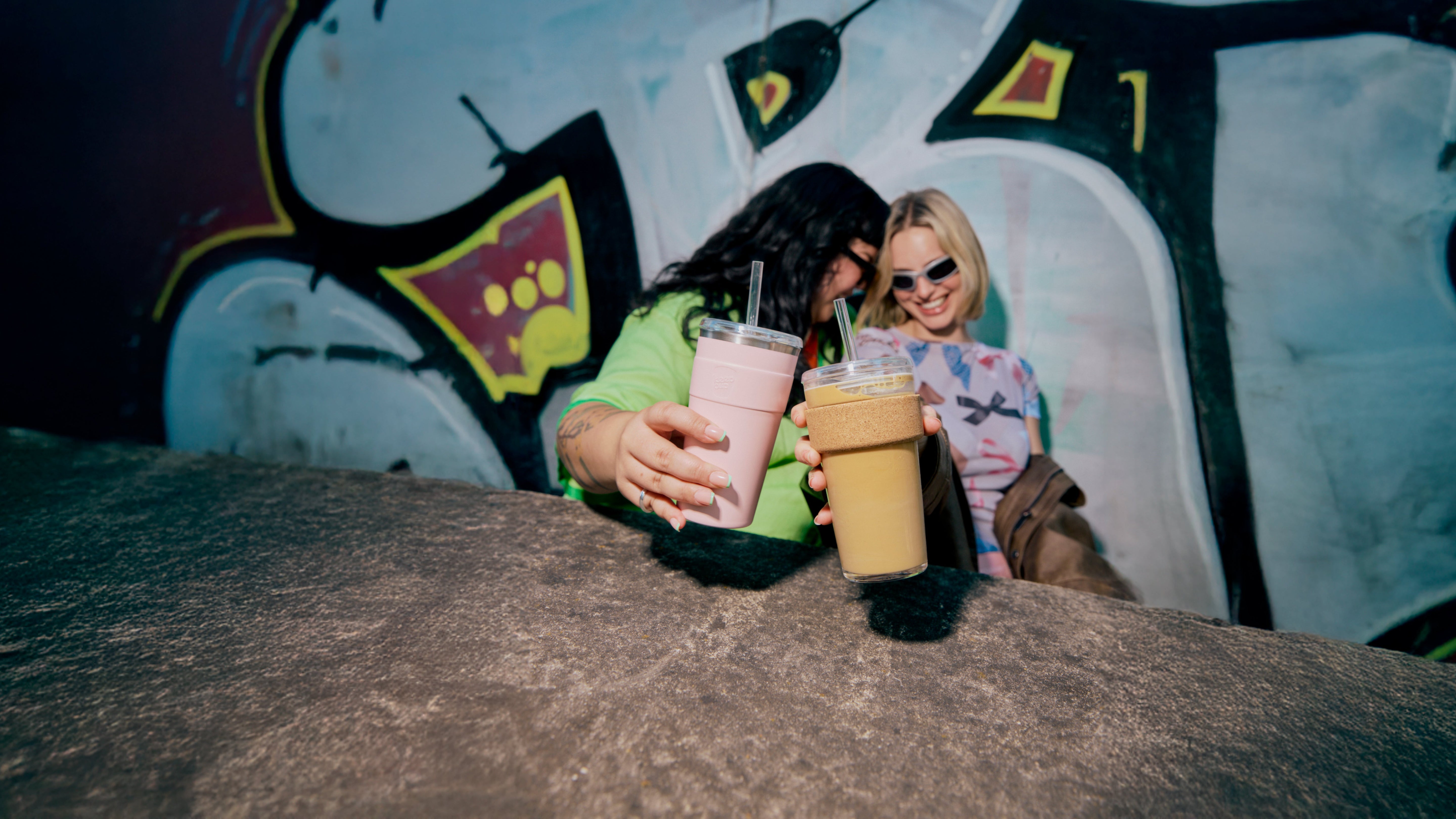 Two people holding drinks in front of a graffiti wall