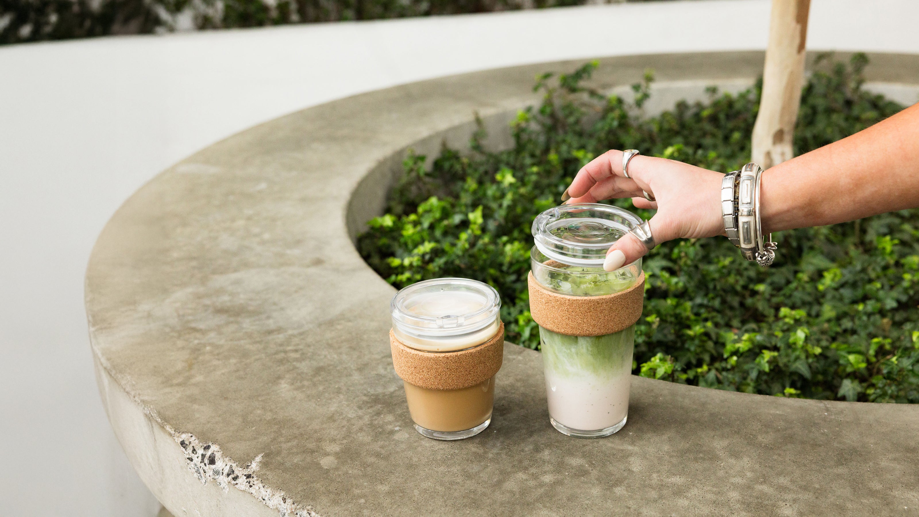 Person holding a glass with a wooden sleeve on a concrete surface with greenery in the background