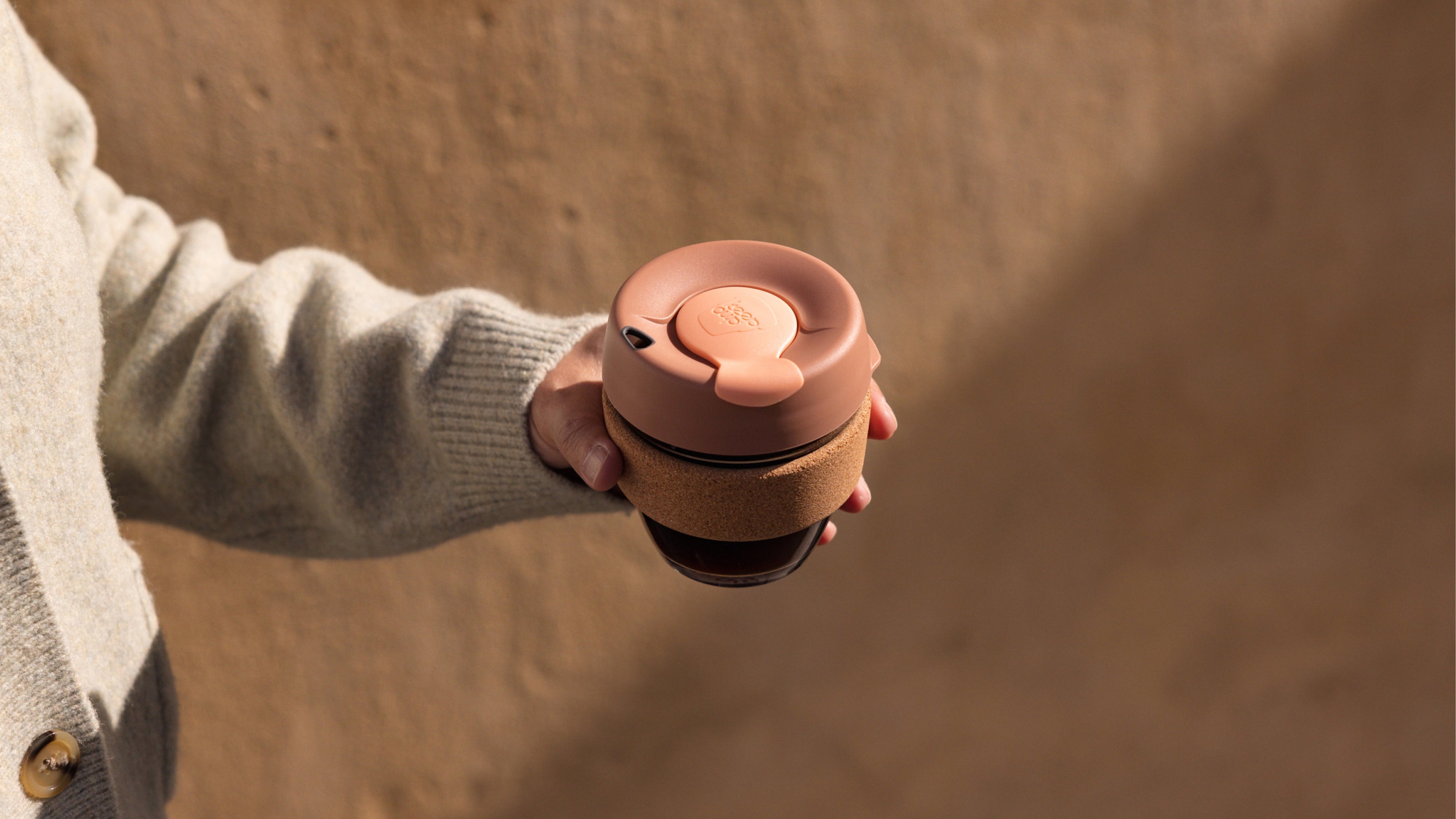 Person holding a pink and brown reusable coffee cup against a blurred background