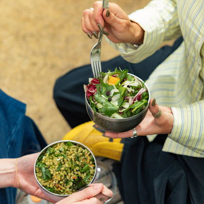 Two people holding bowls of salad outdoors.