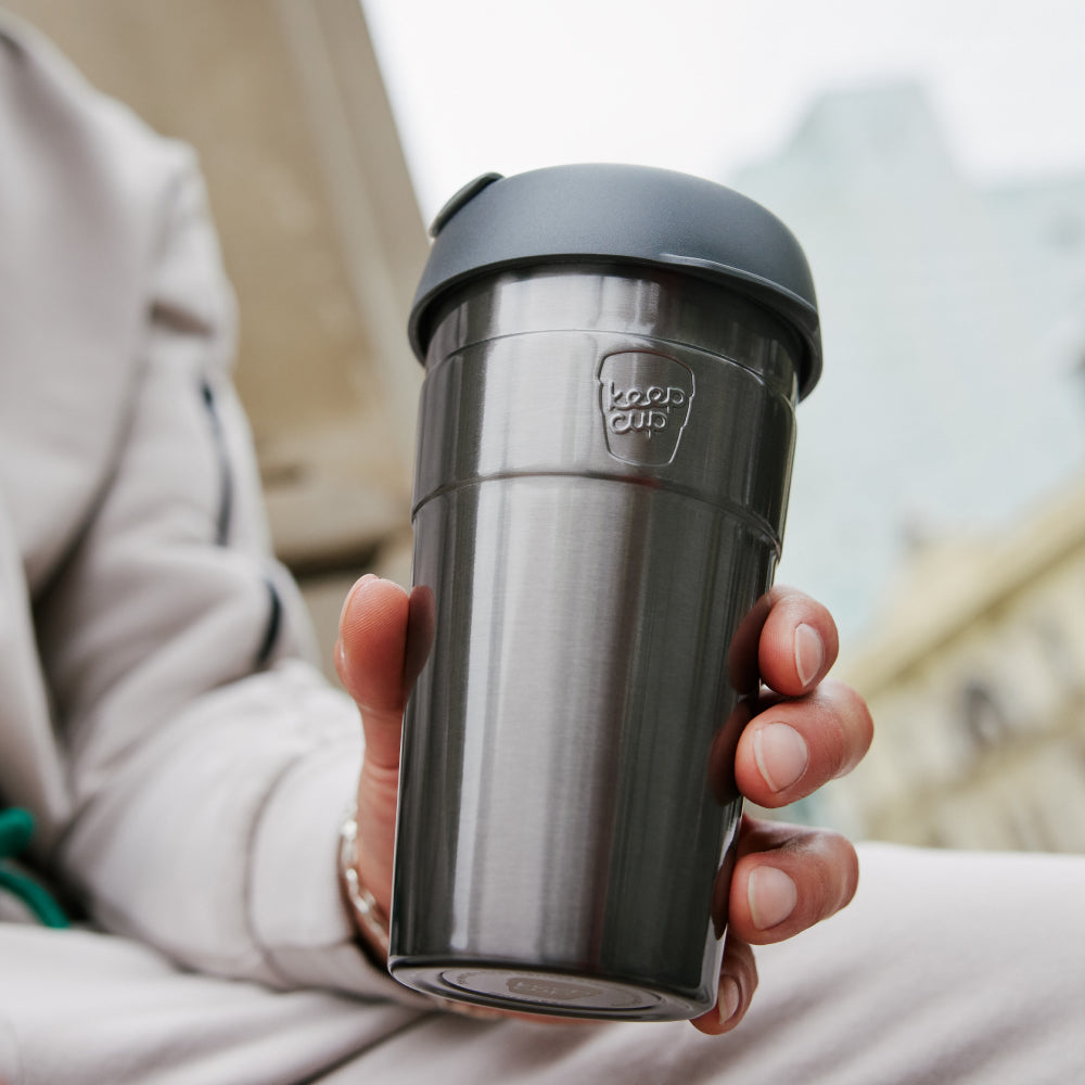 Person holding gray KeepCup reusable coffee cup with black lid outdoors