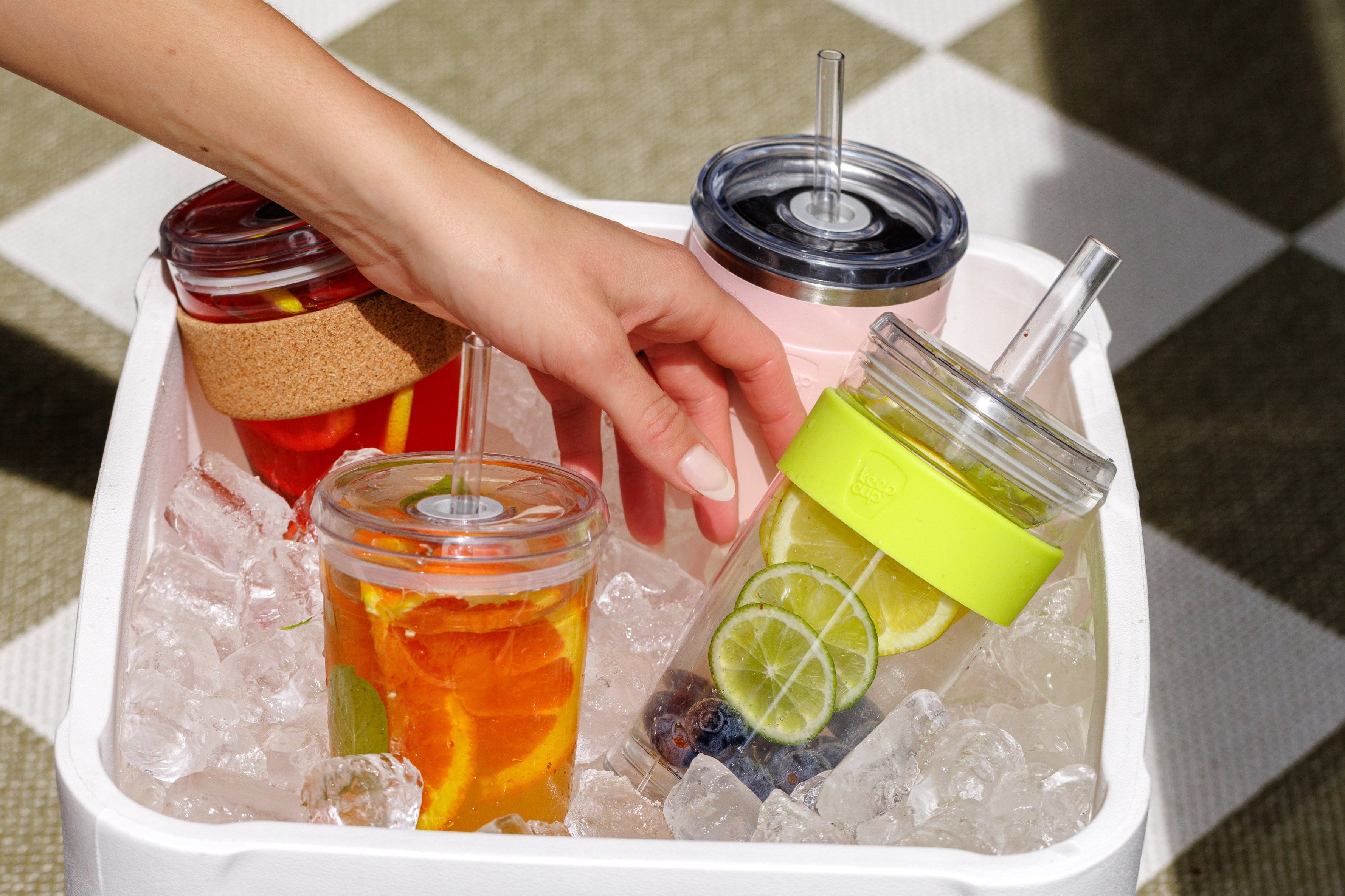 Hand reaching for a drink in a insulated container filled with ice and drinks.