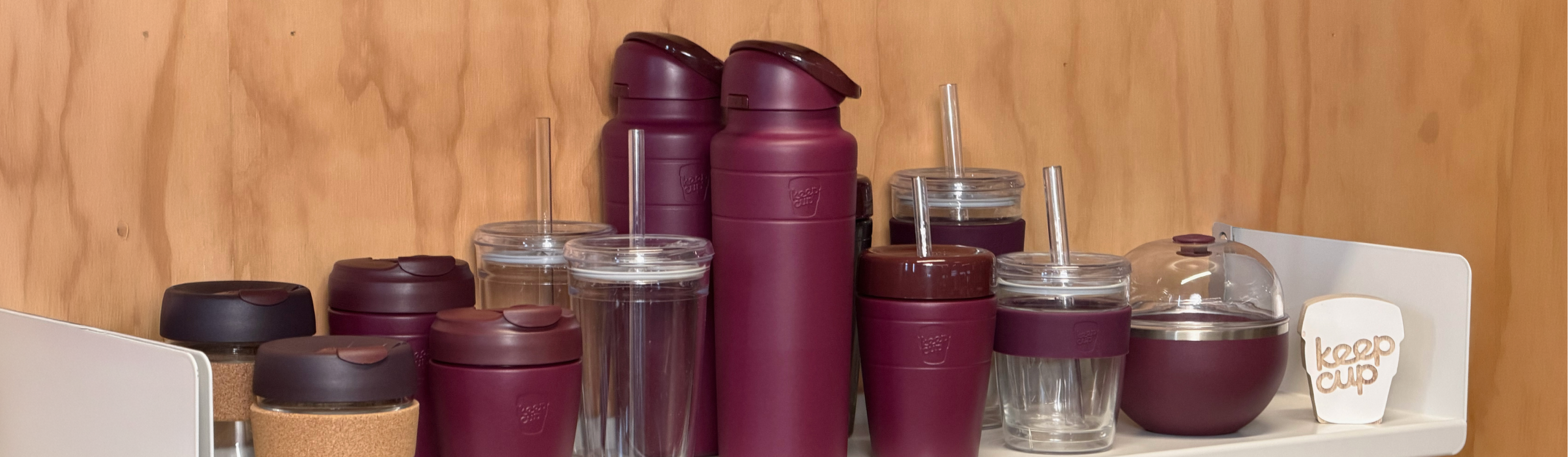 The Mulberry retail range including, Brew Cork, Commuter travel cup, Cold Cup Origjnal, Ora insulated water bottle, Commuter insulated Cold Cup, Cold Cup longplay and Go Bowl Luxe, on a white shelf against a wood-paneled wall.