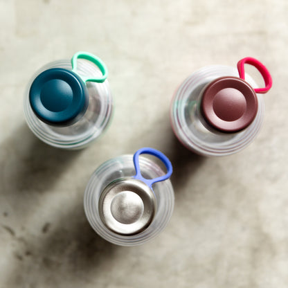 Three clear triran plastic KeepCup water bottles with colorful lids on a marble surface