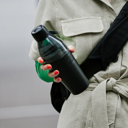 Person holding a black KeepCup water bottle with a beige jacket and red nail polish.