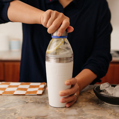 Person putting the lid on a Clear top KeepCup water bottle after filling it with water and a slice of lemon, with a checkered towel and bowl of ice in the background