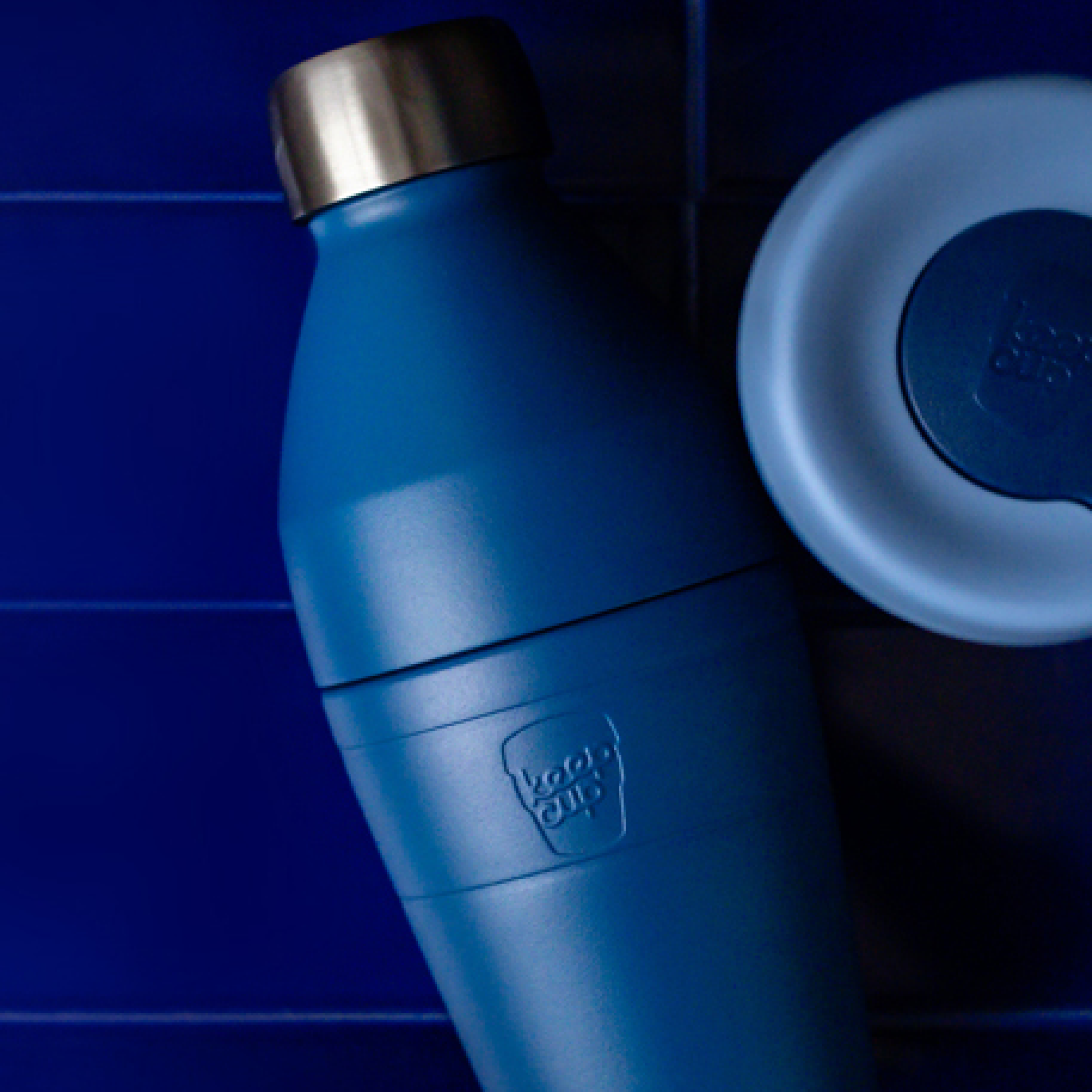 KeepCup blue water bottle with a silver cap, featuring KeepCup traveller lid in matching colourway on a blue background