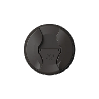 Top-down view of the KeepCup Commuter Flip Lid in Black, showing the circular lid with its curved sipper opening and flip closure embossed with the KeepCup logo.