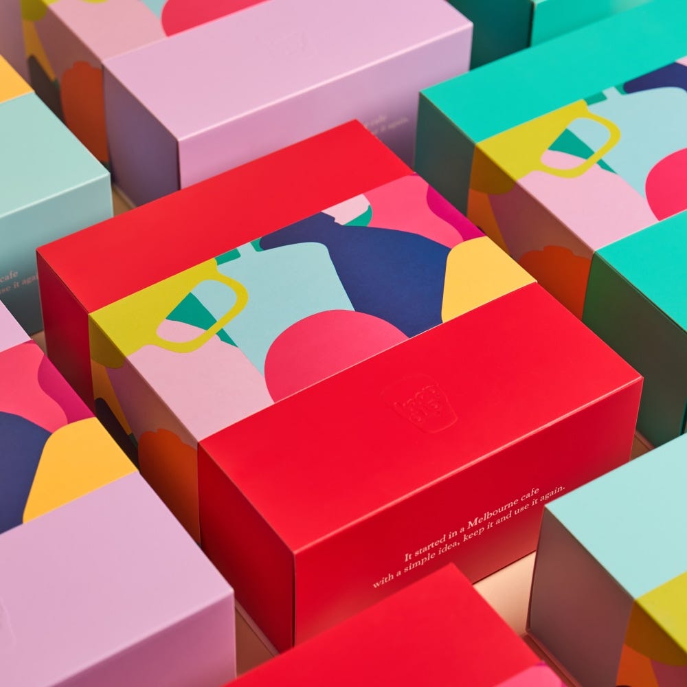 Colorful product packaging boxes for KeepCup Urban Adventurer in Poppy, featuring vibrant abstract designs with reusable cup illustrations in pink, red, teal, and yellow, arranged in a grid pattern with text reading "It started in a Melbourne cafe with a simple idea, keep it and use it again.